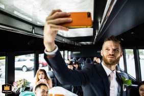 In San Francisco, California, the groom stands at the front of a party bus taking a selfie, while the group of seated guests behind him smile and pose, capturing a candid and energetic post-ceremony celebration.